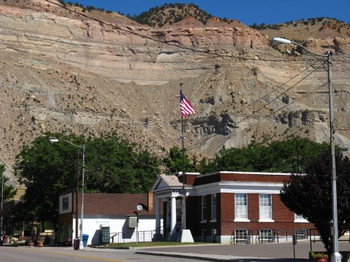 A brick building with an American flag in front, set against a backdrop of rocky cliffs and clear blue sky.