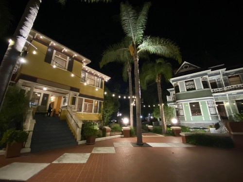 Two charming historic houses illuminated at night, surrounded by palm trees and string lights in a cozy courtyard.