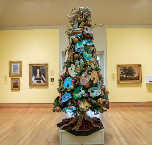 A decorated Christmas tree in an art gallery, surrounded by paintings and featuring colorful ornaments and art palettes.