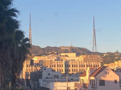View of the Hollywood sign on the mountains, with palm trees and buildings in the foreground.