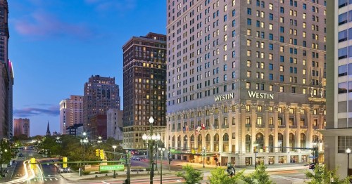 The Westin hotel illuminated at dusk, surrounded by city buildings and busy streets.
