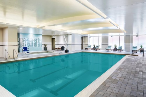 Indoor swimming pool with clear blue water, lounge chairs, and modern decor. Brightly lit with large windows.