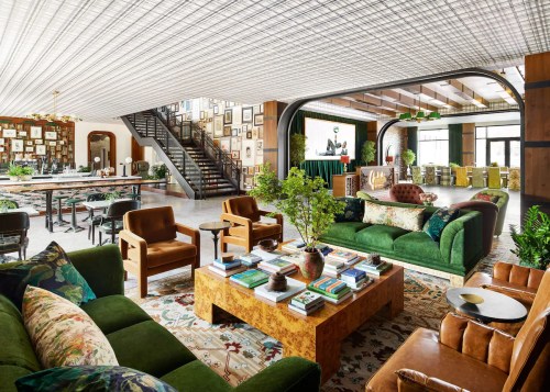 A stylish, modern lounge with green sofas, a wooden coffee table, and a gallery wall, featuring plants and a staircase.