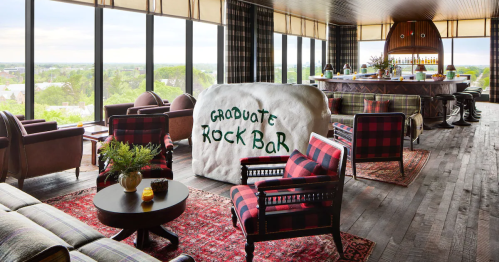 A stylish bar with a rock feature, plaid furniture, and large windows offering a scenic view.
