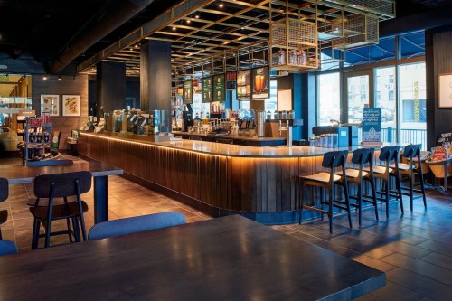A modern coffee shop interior featuring a sleek counter, seating, and large windows with natural light.