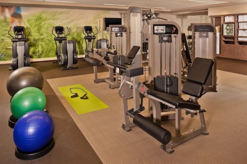 A modern gym interior featuring exercise machines, stability balls, and a yoga mat on the floor.