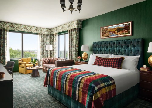 Cozy hotel room with a green theme, featuring a king bed, vintage decor, and large windows with scenic views.