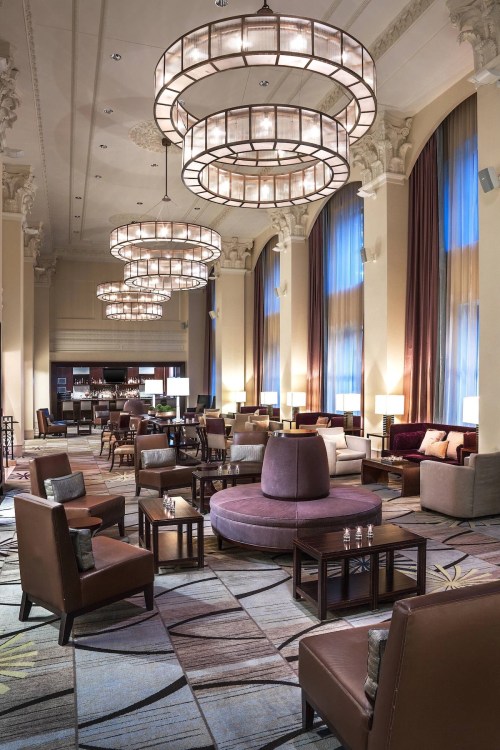 Elegant lounge with plush seating, large chandeliers, and warm lighting, featuring a stylish carpet and bar area.