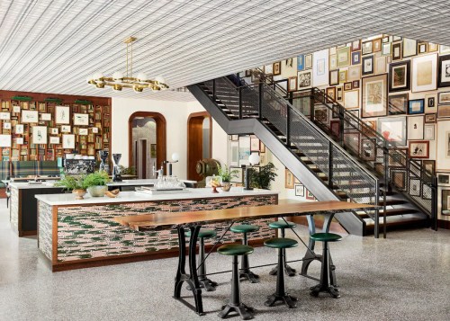 A stylish café interior featuring a bar, seating, and a staircase adorned with framed artwork on the walls.