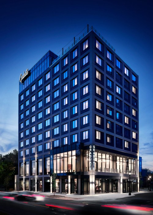 A modern hotel building with a sleek design, illuminated at dusk, featuring large windows and a prominent sign.
