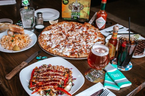A table spread with pizza, salad, mac and cheese, drinks, and condiments in a casual dining setting.