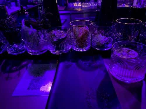 A dimly lit bar with various cocktail glasses and a menu, featuring purple lighting and decorative garnishes.