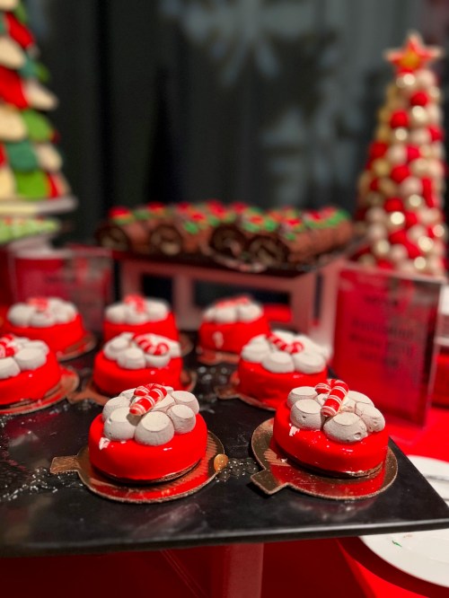 A festive display of red and white desserts, resembling Christmas ornaments, with decorative toppings on a black tray.