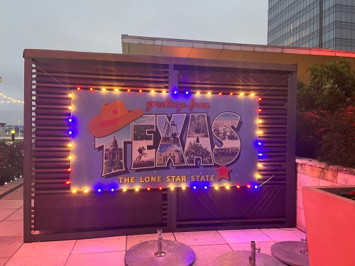 A colorful "Greetings from Texas" sign with lights, featuring a cowboy hat and the phrase "The Lone Star State."