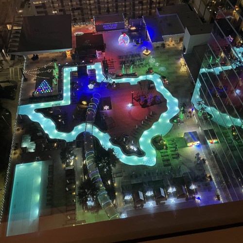 Aerial view of a vibrant pool area with colorful lights, featuring a Texas-shaped pool and various lounge areas.