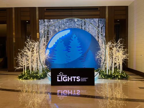 A festive display featuring a large blue orb with trees, surrounded by illuminated branches and a sign for "Texas White Lights."