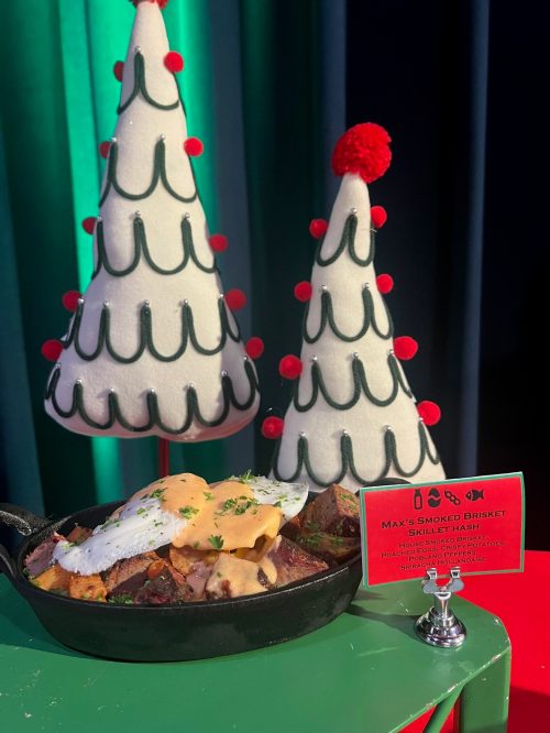 A skillet filled with smoked brisket, topped with cheese and herbs, beside festive Christmas tree decorations.