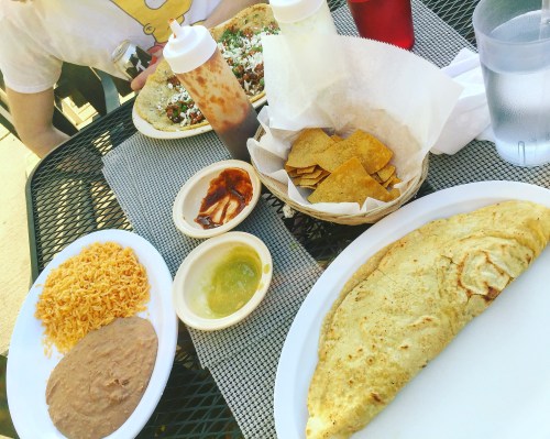 A table with a large omelette, rice, refried beans, chips, and sauces, with drinks in the background.