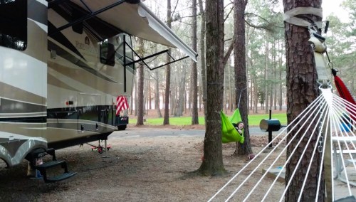 A camper parked among trees, with a hammock set up nearby and a hammock strung between two trees.