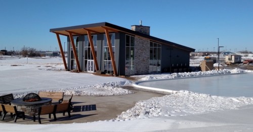 Modern building with large windows, surrounded by snow and ice, featuring a fire pit and outdoor seating area.