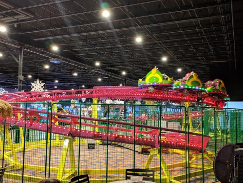 A brightly lit indoor amusement park ride with colorful decorations and a roller coaster track.
