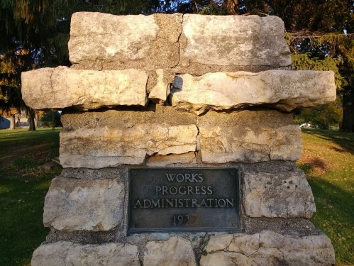Stone monument with a plaque reading "Works Progress Administration 1937," surrounded by greenery.