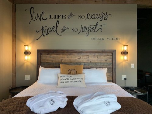 A cozy bedroom featuring a wooden bed, decorative wall art, and plush white robes on the bed.