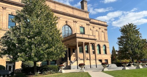 A grand building with a stone facade, large windows, and columns, surrounded by trees and a well-maintained lawn.