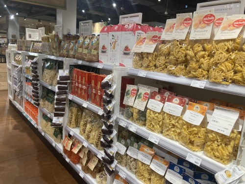 A grocery aisle filled with various types of pasta and packaged food items on shelves.