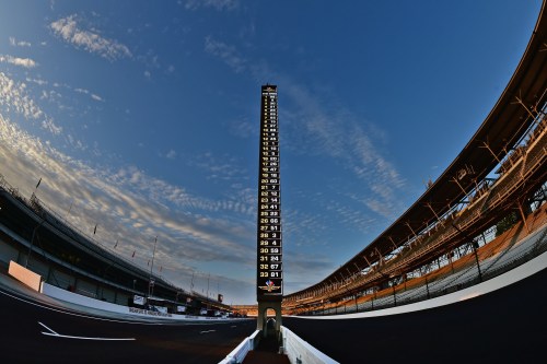 A panoramic view of a racetrack with a tall scoring tower against a blue sky and wispy clouds.