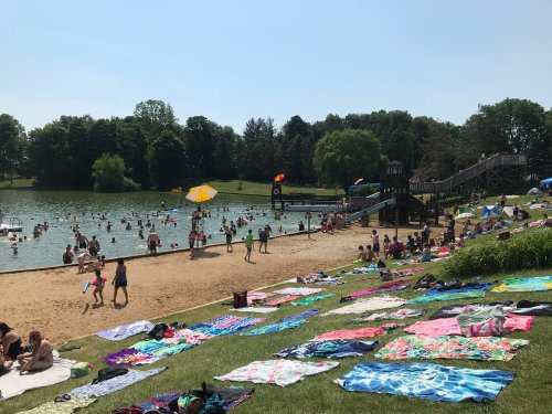 A busy beach area with people swimming, sunbathing on colorful towels, and a playground in the background.