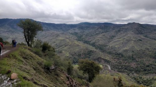 A scenic view of rolling hills and valleys under a cloudy sky, with a hiking trail in the foreground.