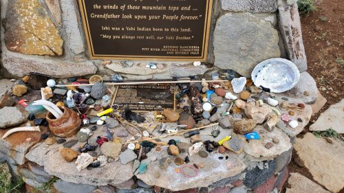 A stone memorial with various items, including rocks, shells, and trinkets, honoring a Yahi Indian ancestor.