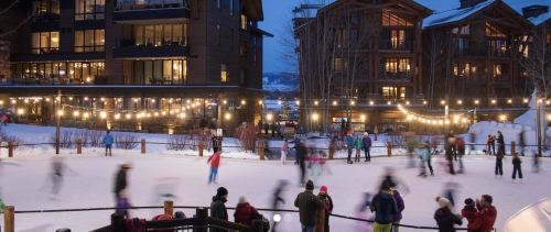 A lively ice skating rink at dusk, surrounded by cozy buildings and twinkling lights, with skaters enjoying the scene.