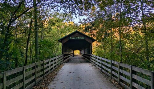 A covered bridge surrounded by trees, leading into a colorful autumn landscape.