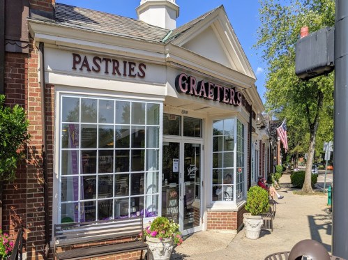 A storefront with large windows displaying pastries, featuring the sign "Graeter's" and an American flag nearby.