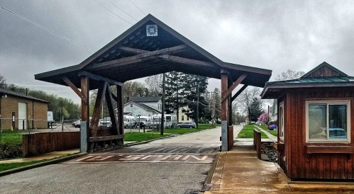 A wooden covered bridge entrance with a blue star emblem, leading to a road lined with trees and buildings.