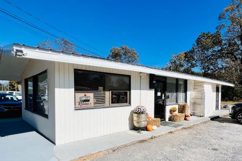 A white building with large windows, featuring a sign for a business, surrounded by pumpkins and fall decorations.