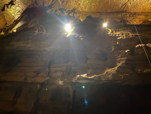 Dimly lit cave interior with textured rock formations and bright lights illuminating the ceiling.