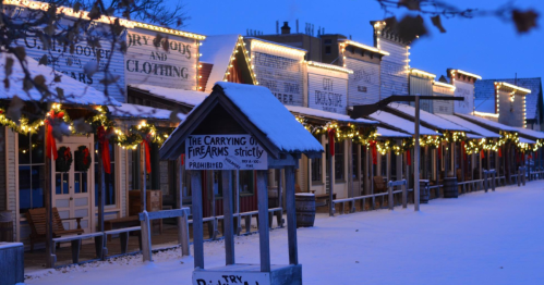 Snow-covered storefronts adorned with holiday lights, creating a festive atmosphere in a quiet, winter scene.