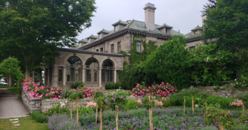 A grand stone mansion surrounded by lush greenery and colorful flower gardens.