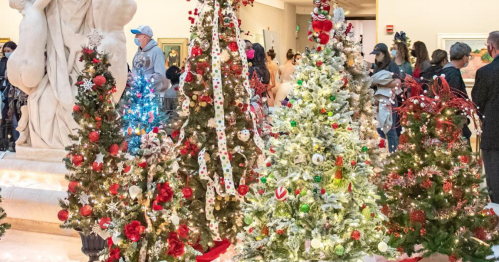 A festive display of decorated Christmas trees in a gallery, with visitors admiring the holiday decorations.