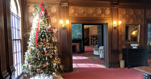 A beautifully decorated Christmas tree stands in a warmly lit room with vintage decor and a red carpet.