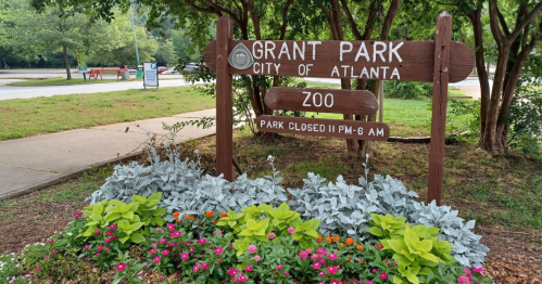 Sign for Grant Park in Atlanta, indicating the zoo and park hours, surrounded by colorful flowers and greenery.