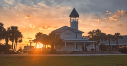 A charming building with a tower silhouetted against a vibrant sunset, surrounded by palm trees.