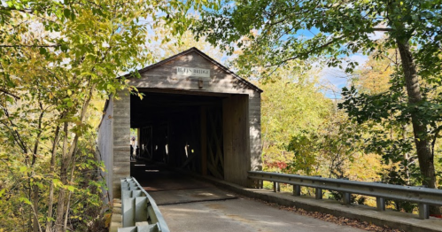 A wooden covered bridge surrounded by colorful autumn trees and a clear blue sky.