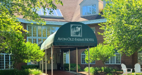 Entrance of Avon Old Farms Hotel with a green awning and lush greenery surrounding the building.