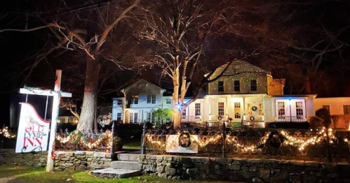 A charming inn decorated with festive lights and wreaths, surrounded by trees, on a quiet night.