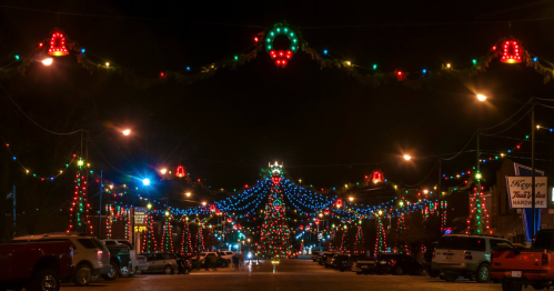 Colorful holiday lights adorn a street at night, creating a festive atmosphere with decorated trees and buildings.