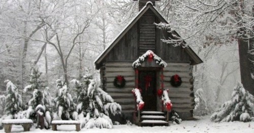 A cozy log cabin adorned with wreaths, surrounded by snow-covered trees in a winter landscape.
